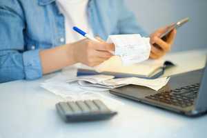 Woman going through bills and receipts with calculator, phone and laptop