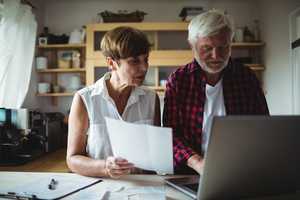 Older couple with paperwork and a laptop, paying bills online