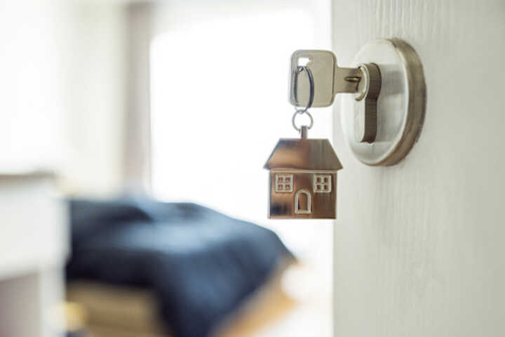 An open door with a key in the lock on a house-shaped keyring